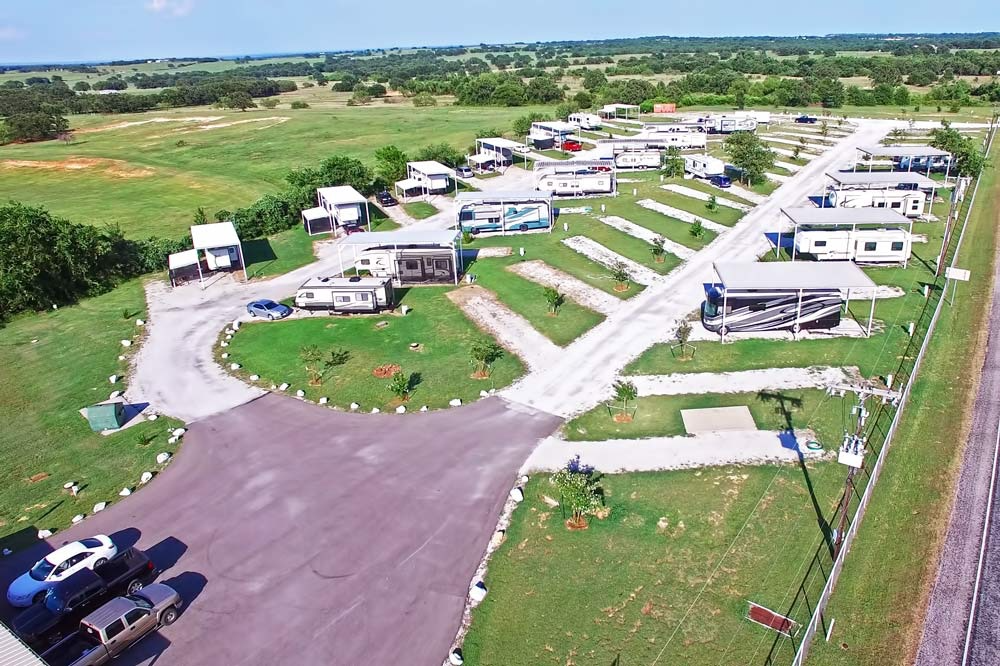 Aerial View of a Rural RV Park – A neatly arranged RV park in a scenic rural setting, featuring covered RV sites and open parking areas, designed for extended stays and comfortable accommodations.