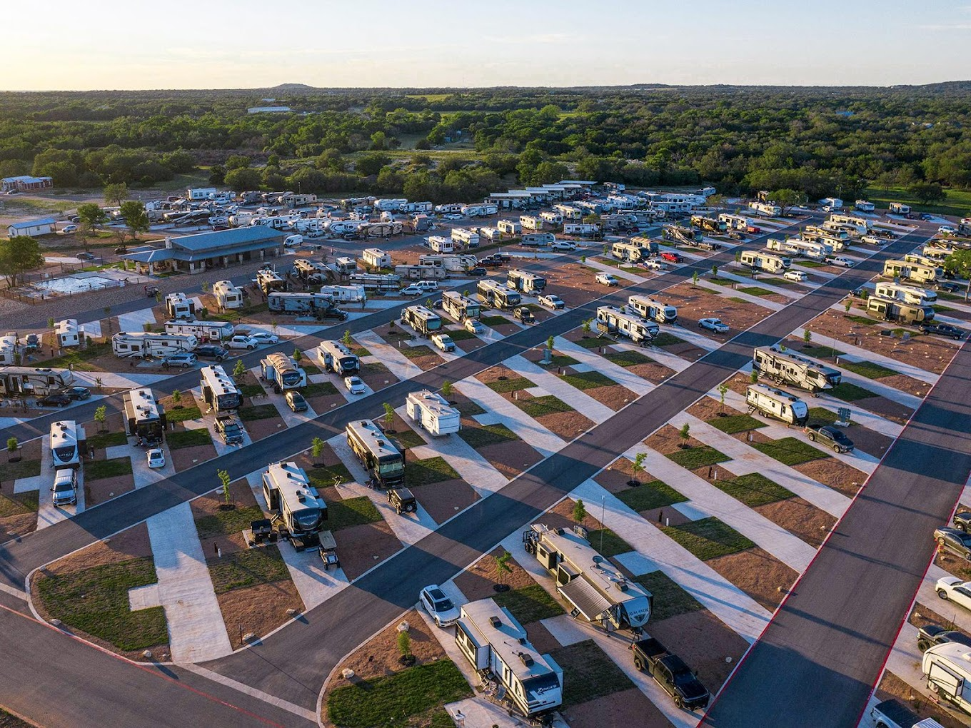 Aerial View of a Large RV Park – A well-organized RV park with paved driveways, modern amenities, and a mix of covered and uncovered sites. Surrounded by greenery, this park is designed for extended stays and convenience.