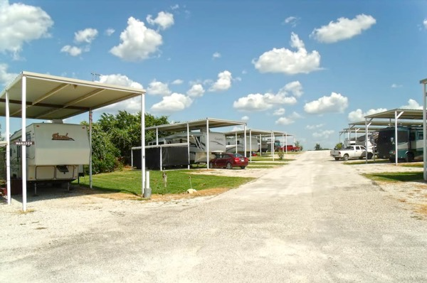 Row of Covered RV Sites – A lineup of RVs parked under covered structures, providing shade and protection. The gravel road and open landscape create a quiet, practical setting for long-term residents.