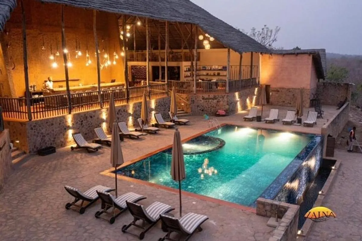 A luxurious outdoor pool area at Zaina Lodge in Ghana, featuring an infinity-edge pool, lounge chairs, and an open-air bar with ambient lighting. Zaina Lodge exemplifies high-end glamping with an African safari experience, a model that Sage Outdoor Advisory considers when conducting a feasibility study for outdoor hospitality developments.