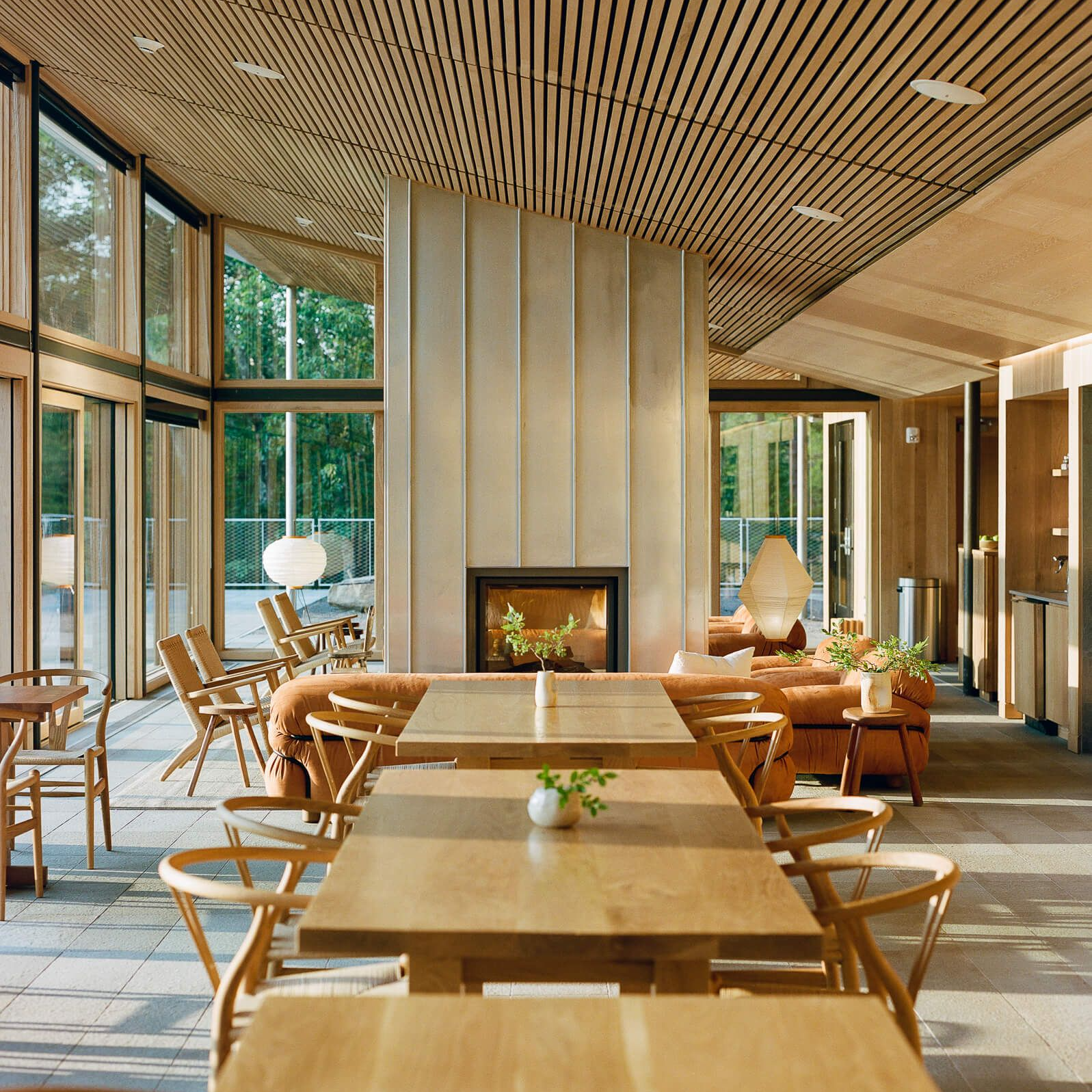 A warm, minimalist dining and lounge space featuring natural wood tones, soft lighting, and a sleek fireplace. This eco-luxury setting fosters a serene ambiance, seamlessly connecting guests with the surrounding landscape. Blog post by Sage Outdoor Advisory, offering Glamping and RV Feasibility Studies