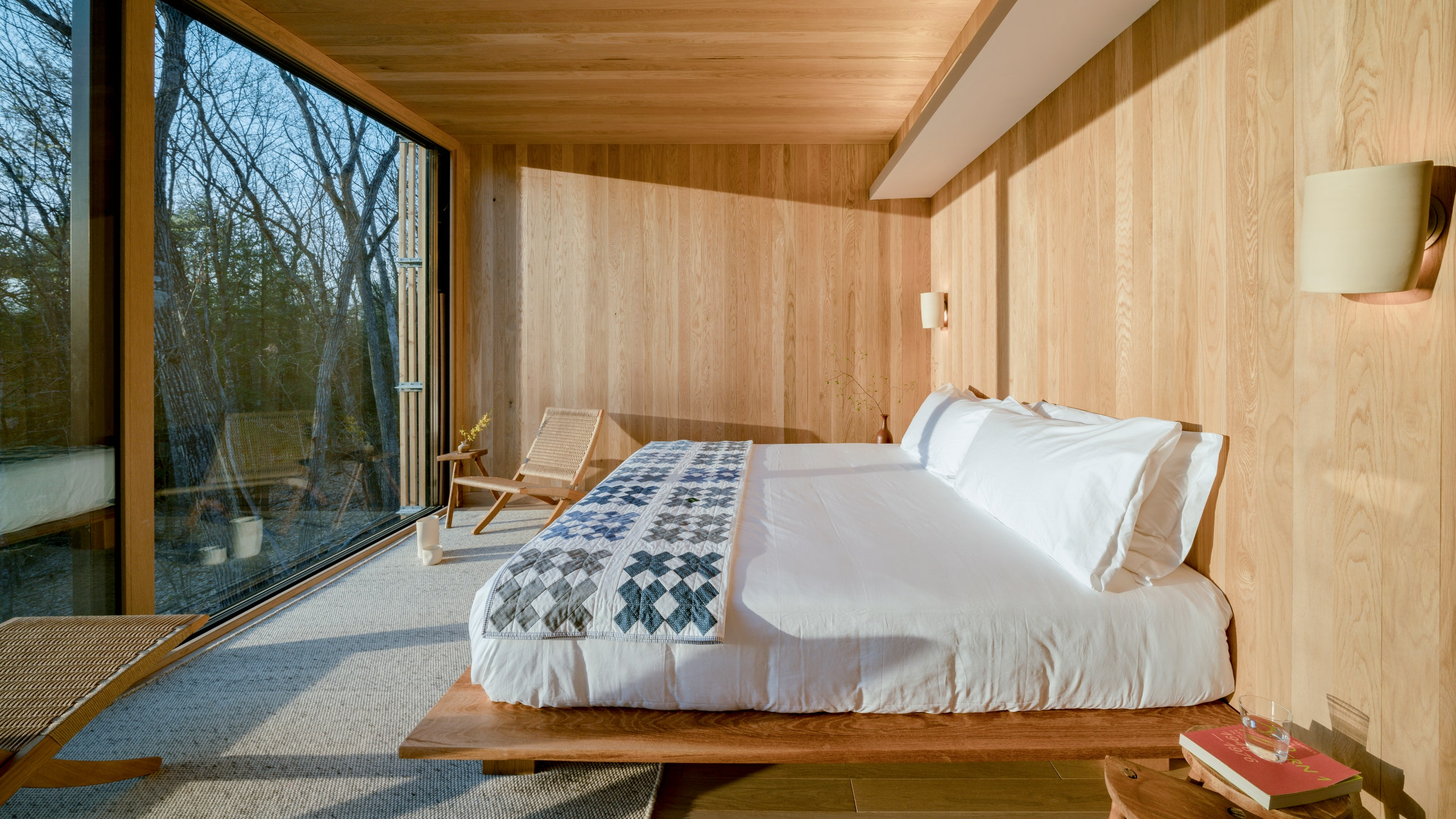 A serene bedroom at a luxury landscape hotel, featuring minimalist Japandi-inspired design with warm wood tones, floor-to-ceiling windows, and natural light. This eco-conscious retreat blends modern comfort with nature for a peaceful escape.