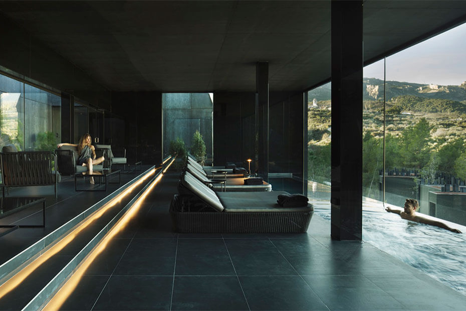 A sleek, modern spa lounge with dark, minimalist interiors and panoramic glass walls overlooking a rugged natural landscape. This tranquil retreat offers a luxurious and immersive relaxation experience in a remote setting. Blog post by Sage Outdoor Advisory, offering Glamping and RV Feasibility Studies