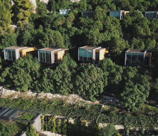 A stunning aerial view of a landscape hotel seamlessly integrated into lush greenery. These elevated glass-fronted suites offer an eco-conscious retreat, blending modern architecture with nature for an immersive stay in the wilderness. Blog post by Sage Outdoor Advisory, offering Glamping and RV Feasibility Studies