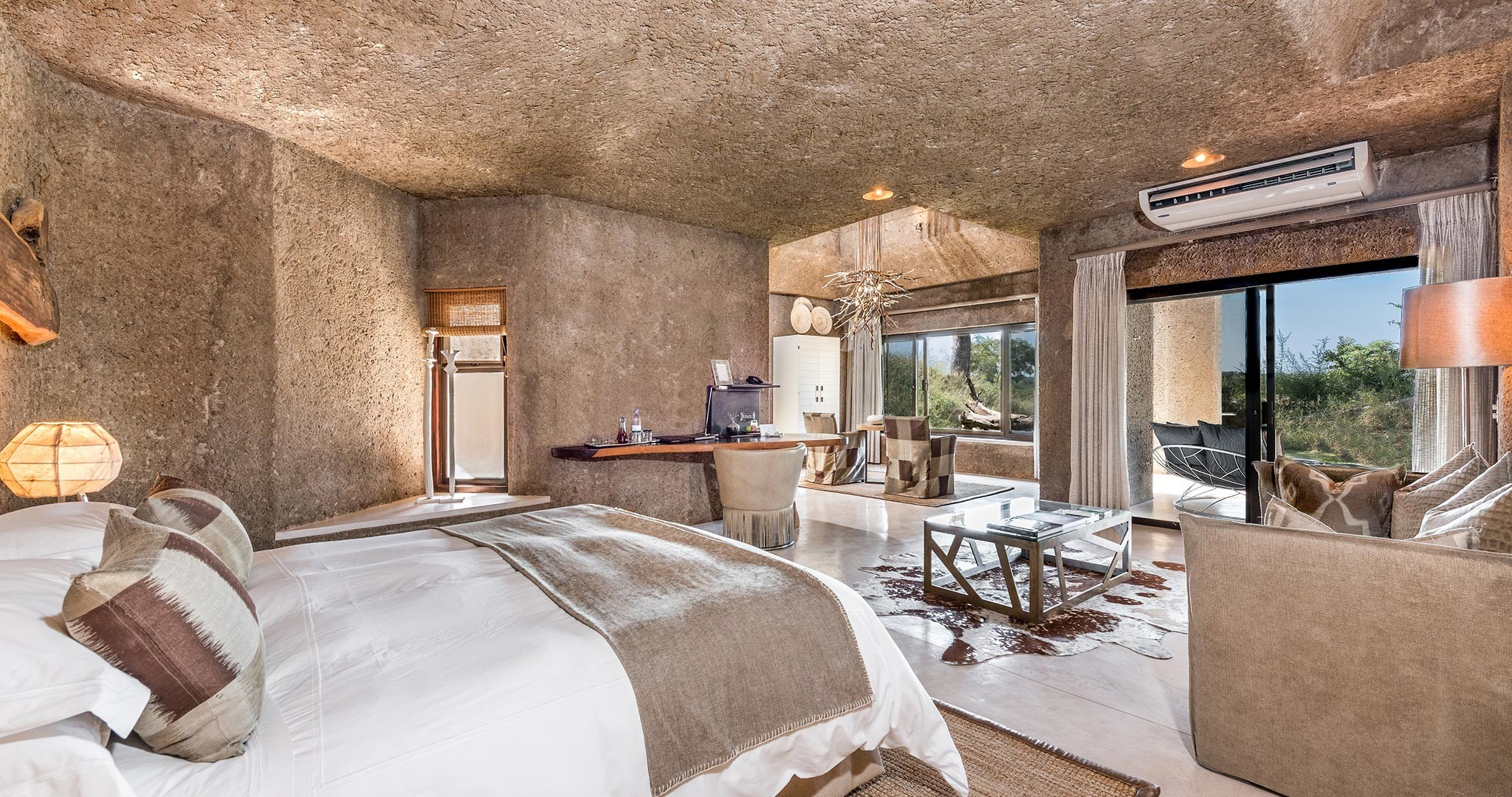 A luxurious safari lodge suite with a modern, earth-toned interior, featuring natural textures, an open floor plan, and expansive glass doors leading to a private terrace with scenic views. Sage Outdoor Advisory conducts feasibility studies for high-end glamping accommodations like this.