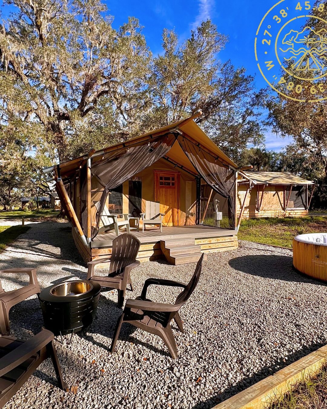 A luxurious glamping tent at Peace River Oaks, featuring a wooden deck with Adirondack chairs, a fire pit surrounded by gravel, and a hot tub nearby. The tent is set among tall oak trees with Spanish moss under a bright blue sky. Sage Outdoor Advisory helps outdoor hospitality businesses like Peace River Oaks grow with expert feasibility studies and strategic insights.
