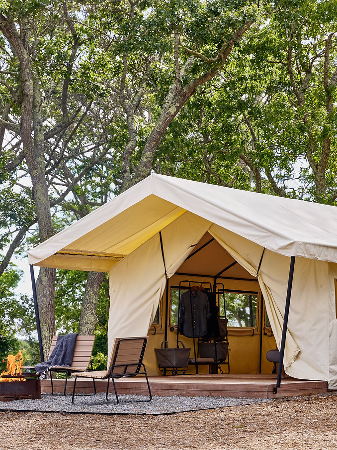 Safari-style glamping tent nestled in a wooded setting, featuring a canvas structure, front porch with lounge chairs, and a cozy fire pit. This image captures the appeal of outdoor hospitality and the type of accommodations evaluated in Sage Outdoor Advisory’s glamping feasibility studies and market reports for investors and developers.