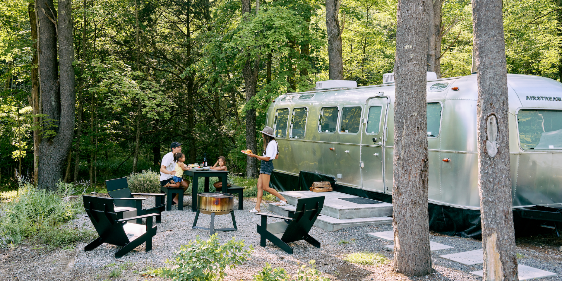 Family enjoying outdoor dining next to an Airstream trailer in a wooded glamping resort—highlighting guest experiences evaluated in a Sage Outdoor Advisory glamping feasibility study.