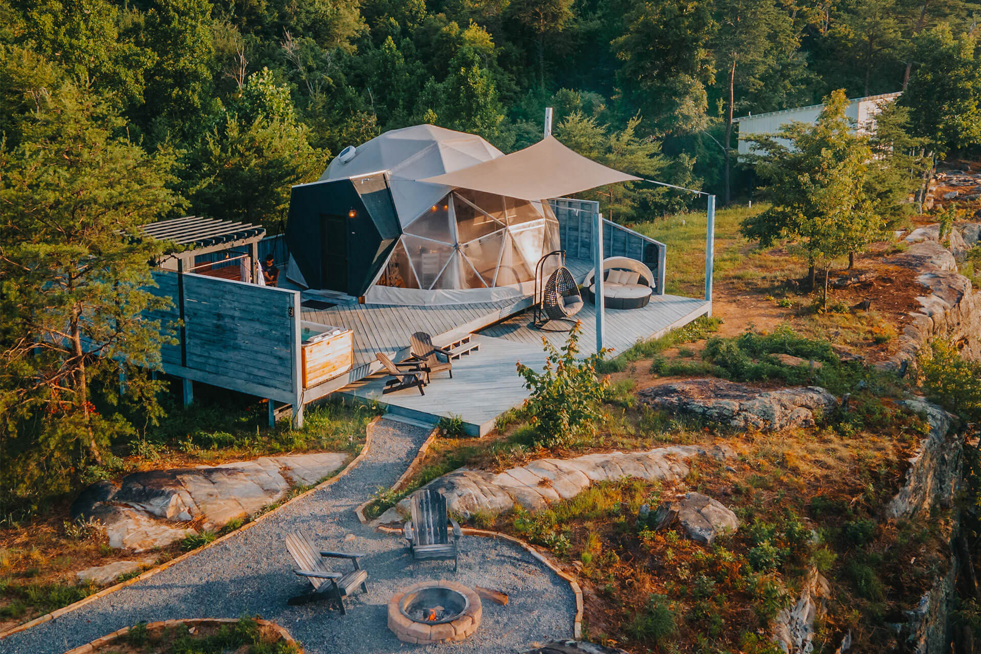 A scenic glamping geodesic dome nestled amidst lush greenery, featuring a spacious wooden deck, outdoor seating, fire pit area, and modern amenities, providing a luxurious camping experience. This image reflects the kind of unique glamping concepts assessed through Feasibility Studies conducted by Sage Outdoor Advisory, experts in the outdoor hospitality industry.
