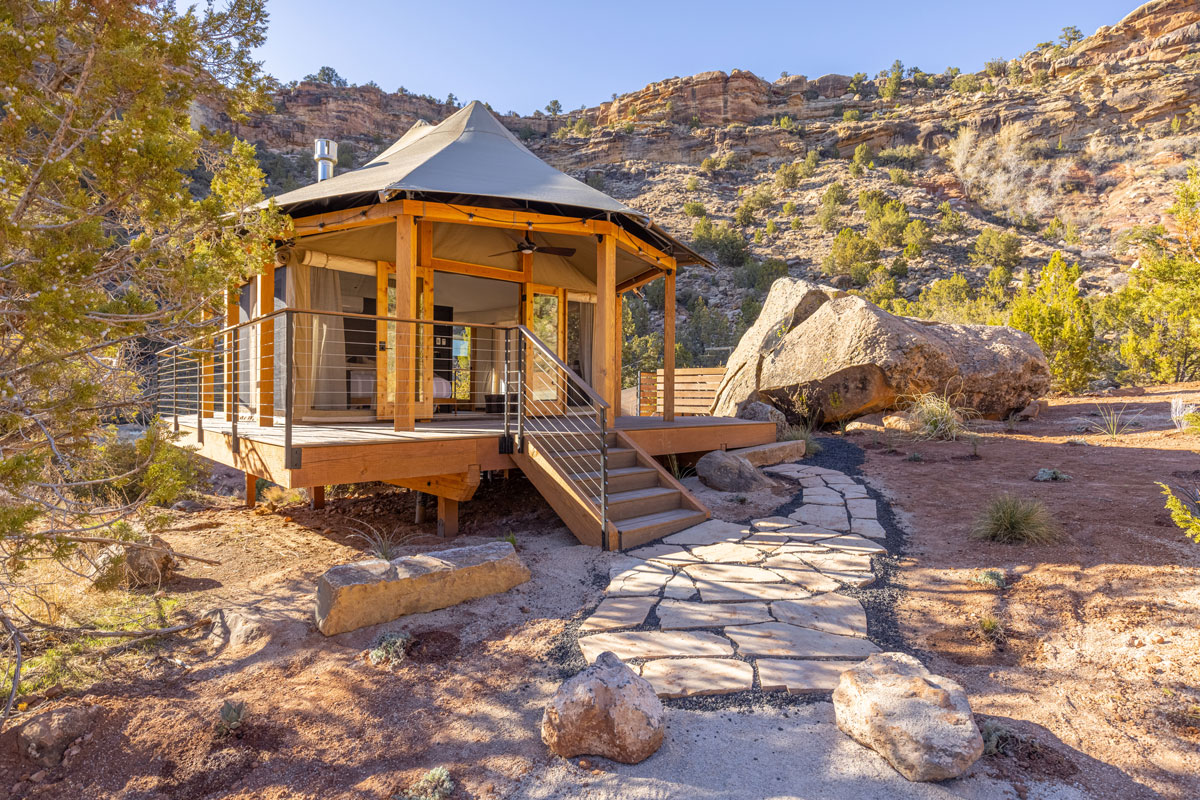 Premium glamping tent elevated on a sturdy wooden platform, featuring expansive windows and doors, set against a stunning backdrop of dramatic cliffs and rocky desert terrain. Sage Outdoor Advisory's detailed Feasibility Studies help investors confidently pursue distinctive, upscale glamping projects.