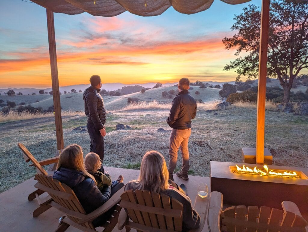 Guests relaxing around a fire pit while watching the sunset from a glamping deck—an experience Sage Outdoor Advisory analyzes when evaluating emotional appeal and guest value in feasibility studies.