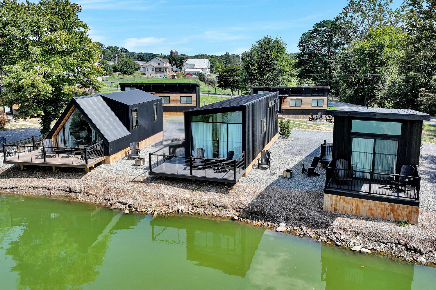 A collection of sleek, modern tiny homes and cabins with black exteriors and private decks overlooking a tranquil pond, arranged in a clean, minimalist layout. Sage Outdoor Advisory includes contemporary units like these in Feasibility Studies to evaluate revenue potential and site planning in glamping resort developments.
