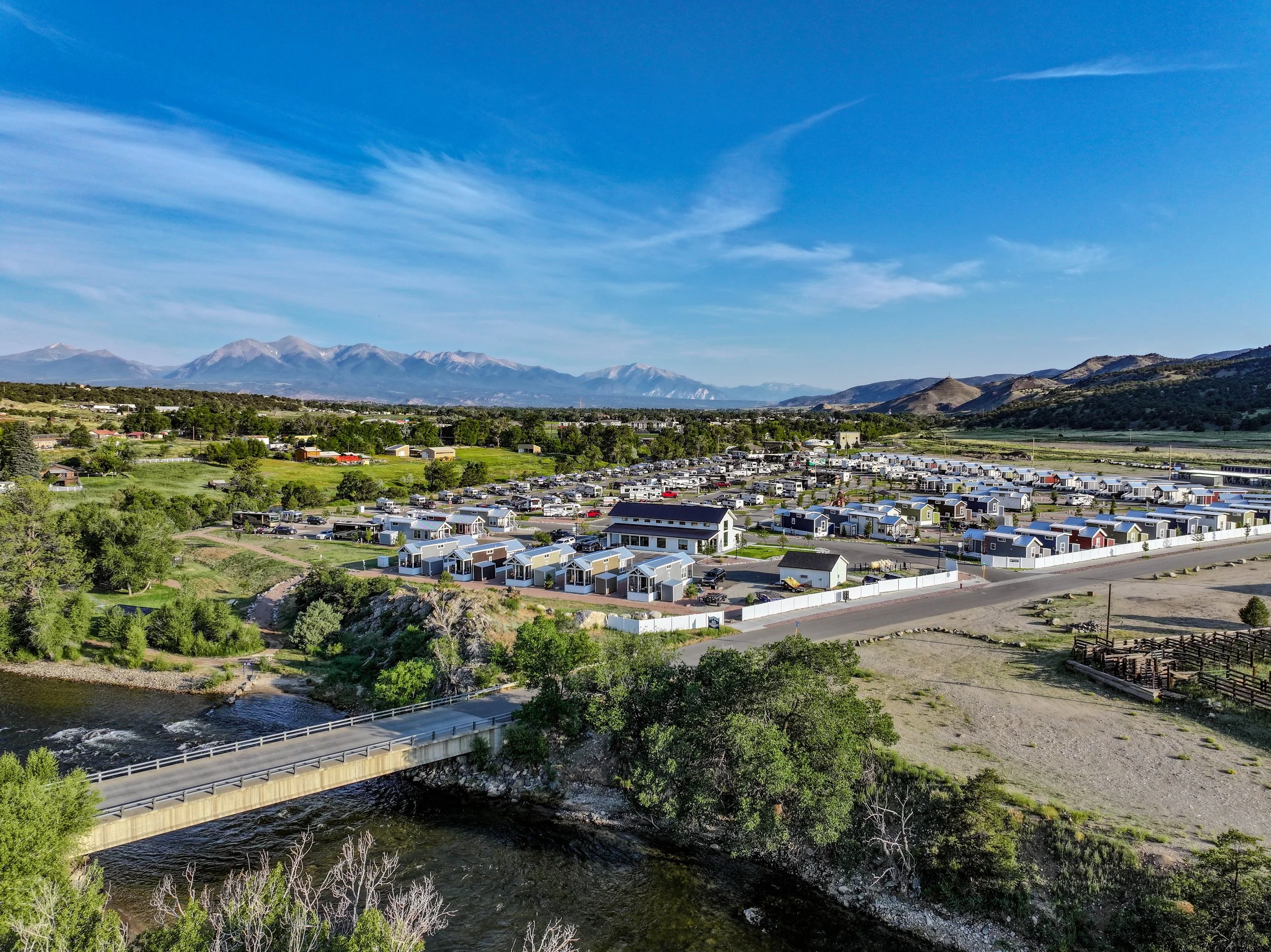 Aerial view of Salida RV Resort in Colorado with tiny homes, RV sites, and the Arkansas River in the foreground, backed by mountain ranges. Sage Outdoor Advisory supports resorts like this through feasibility studies, appraisals, and consulting to ensure strong financial performance and market alignment.