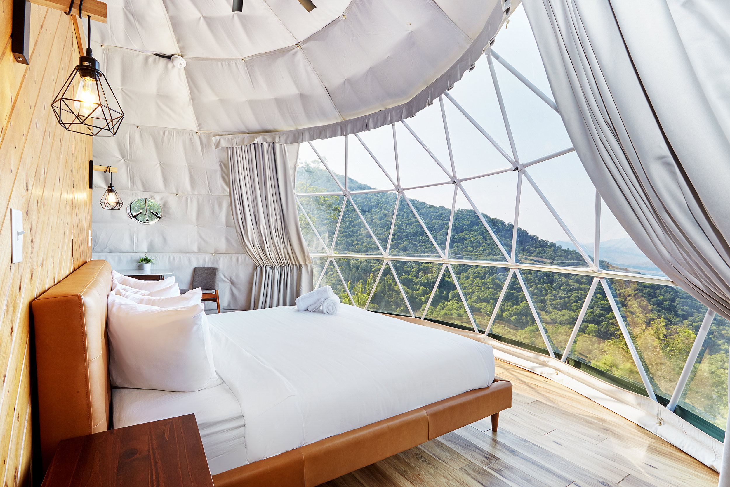 Interior of a dome glamping unit with king-size bed and panoramic mountain views. Sage Outdoor Advisory helps investors through consulting, feasibility studies, and market research.