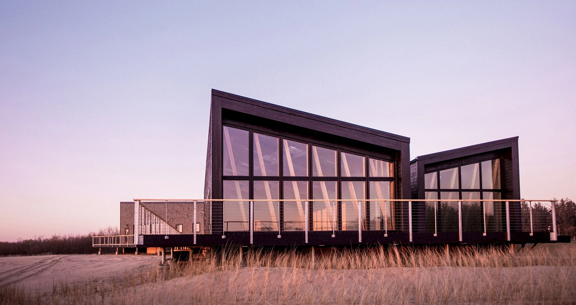 Contemporary coastal cabins with angular design and floor-to-ceiling glass at sunset along the beach. Sage Outdoor Advisory delivers appraisals, feasibility studies, and consulting to align glamping and outdoor resort concepts like this with operational strategy and market demand.