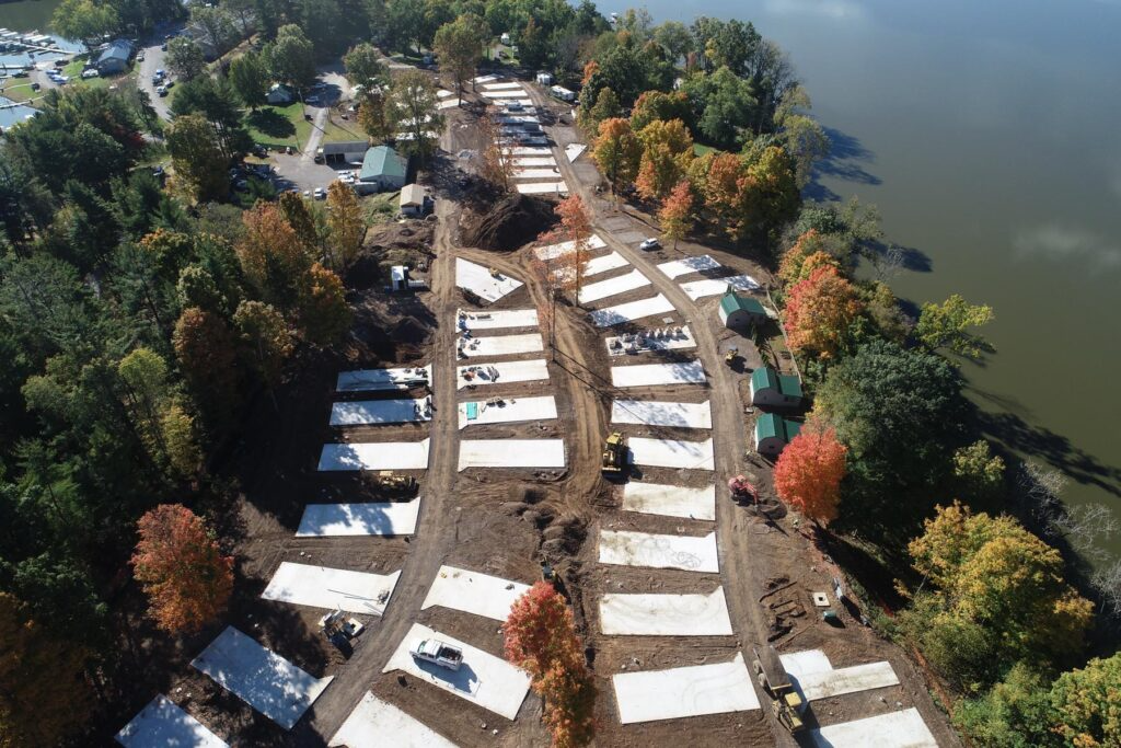Drone photo looking down on the Charles Mill Lake Park campground redevelopment, featuring rows of newly poured concrete RV pads along two main access roads, construction equipment on-site, and fall-colored trees bordering the lakeshore.